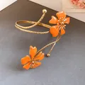 Detail view of an elegant gold armlet featuring two vibrant orange enamel flowers. - Orange