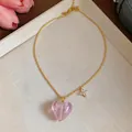 Detail view of a gold-plated heart necklace with a pink glass pendant and flower charm - Necklace / Pink