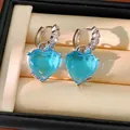 Close-up of silver-tone hoop earrings featuring large light blue heart-shaped crystals. - Heart Letter Hoop Earring (HE33916) / Blue