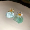 Close-up of sweet summer floral stud earrings with light green translucent shell discs - Blue