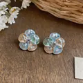 Detailed view of elegant colorful glazed flower stud earrings on a rustic wooden surface. - Blue and Green Patchwork