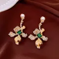Detail of floral gold earrings featuring emerald center stones and pearl accents - Style 6