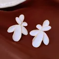 Detail view of elegant white petal flower stud earrings with gold trim on dark fabric - Style 7