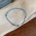 Detail of a light blue woven cord bracelet with a silver fish charm and beads - Blue