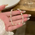 Detailed view of a dainty pearl bracelet with shimmering cubic zirconia star charms held in hand. - Gold