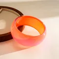 Detail view of a chunky resin bangle with orange and glittery pink gradient. - Orange