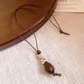 Detailed view of a vintage ethnic style resin pendant on a long brown cord necklace. - Water Drop Pendant Style