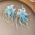 Detailed macro shot of elegant white floral earrings with blue and yellow beaded tassels - Silver Needle / Blue