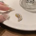 Close-up detail of a French style zircon and pearl multi-layer ear cuff on a plate - Single Ear Clip / Gold