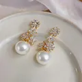 Close-up of elegant French floral earrings with sparkling zircons and white pearls. - Gold
