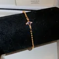 Elegante bracciale dorato con zircone a rombo centrale su supporto di velluto nero. - Stile Croce Viola / Oro