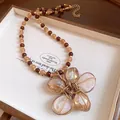 Dettaglio ravvicinato di una collana vintage con ciondolo fiore in vassoio di legno - Marrone