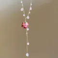 Close-up of elegant gold necklace with pink stones and dried rose pendant detail. - Pink