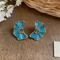 Close-up of blue enamel fan-shaped earrings with rhinestones on a wooden background - Blue