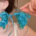 Detail view of blue iridescent shell earrings with satin ribbon bows for a summer look - Bow Shell Tassel Style