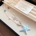 Vista detallada de un collar con colgante de estrella de mar azul claro en un joyero. - Azul