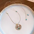 Detailed view of a round openwork pendant with colorful natural stones on a tan cord - Blue
