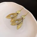 Detailed macro close-up of vintage textured gold leaf-shaped dangle earrings on plate - Gold