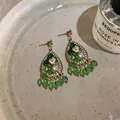 Close-up of green teardrop earrings with floral design, crystals and bead dangles. - Green