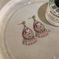 Close-up of ornate water-drop earrings featuring sparkling crystals and pink beads on a plate - Pink