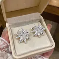 Close-up view of elegant silver-colored zircon flower stud earrings in a cream jewelry box - Silver