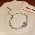 Dettaglio di un bracciale di perle a farfalla placcato oro 18 carati su un piatto crema - Argento