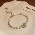 Dettaglio di un ciondolo a farfalla placcato oro 18k su un braccialetto di perle e zirconi - Oro