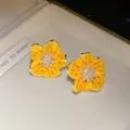 Dettaglio macro di orecchini a lobo a fiore in smalto giallo con zirconi e perle - Giallo
