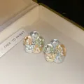 Dettaglio macro di orecchini a lobo a fiore con petali in smalto e zircone centrale - Blu-Marrone-Verde