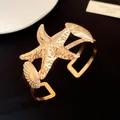Detailed view of a shiny gold starfish and seashell metal cuff bracelet on black - Bangle / Gold