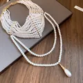 Dettaglio elegante di una collana di perle a più fili con un pendente a goccia classico. - Bianco