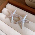 Detailed macro shot of elegant pearlized starfish earrings on a soft beige velvet jewelry display - Earrings / White
