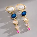 Close-up of elegant gold-tone dangle earrings with teardrop pearls and multi-color crystals - Earrings / Gold Blue White