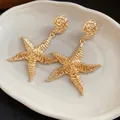 Primo piano di orecchini a stella marina dorati con trama plissettata - Oro