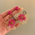 Vista dettagliata di orecchini a fiore in rafia rosa con montatura dorata - Rosa Rosso