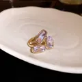Vista dettagliata di un anello aperto dorato con tre scintillanti cristalli ovali viola chiaro - Rosa