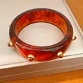 Vista dettagliata di un bracciale in resina con effetto marmo ambra e rivetti dorati lucidi - Bracciale(HB6151) / Marrone