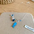 Detailed close-up of a blue resin fish pendant on a clear beaded necklace for women. - Blue