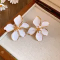 Close-up view of elegant white enamel flower earrings resting in a wooden jewelry box - Silver Needle Flower Style / White