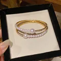 Close-up of elegant gold bangle featuring radiant pearls and sparkling rhinestone inlay. - Gold/White
