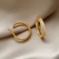 Eleganti orecchini a cerchio dorati con zirconi incastonati su sfondo di seta - Oro