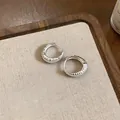 Dettaglio di orecchini a cerchio a U argentati con trama rigata su sfondo in tessuto beige - Argento