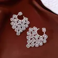 Dettaglio di orecchini geometrici di lusso in zircone su sfondo in tessuto marrone - Argento