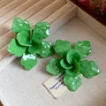 Primer plano de pendientes de flores esmaltadas en verde en un joyero de terciopelo - Verde