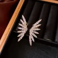 Macro view of 18k gold plated wing-shaped ear clips set with sparkling cubic zircons. - Clip-On Earrings / Gold