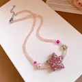 Gros plan d'un collier de perles roses détaillant l'étoile pailletée et la perle douce - Collier