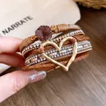 Dettaglio macro di un bracciale in pelle multistrato boho con cuore dorato e cristalli. - Colore Caffè - Cuore