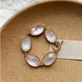 Vista dettagliata di un bracciale bohémien dorato con pietre ovali in resina e chiusura a T - Oro-Bianco