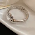 Dettaglio macro del bracciale rigido incrociato a goccia in metallo argento minimalista - Cerniera a Molla Incrociata (8#)