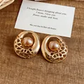 Detailed view of gold hollow-out stud earrings with central champagne pearl inlay - Gold / Gold